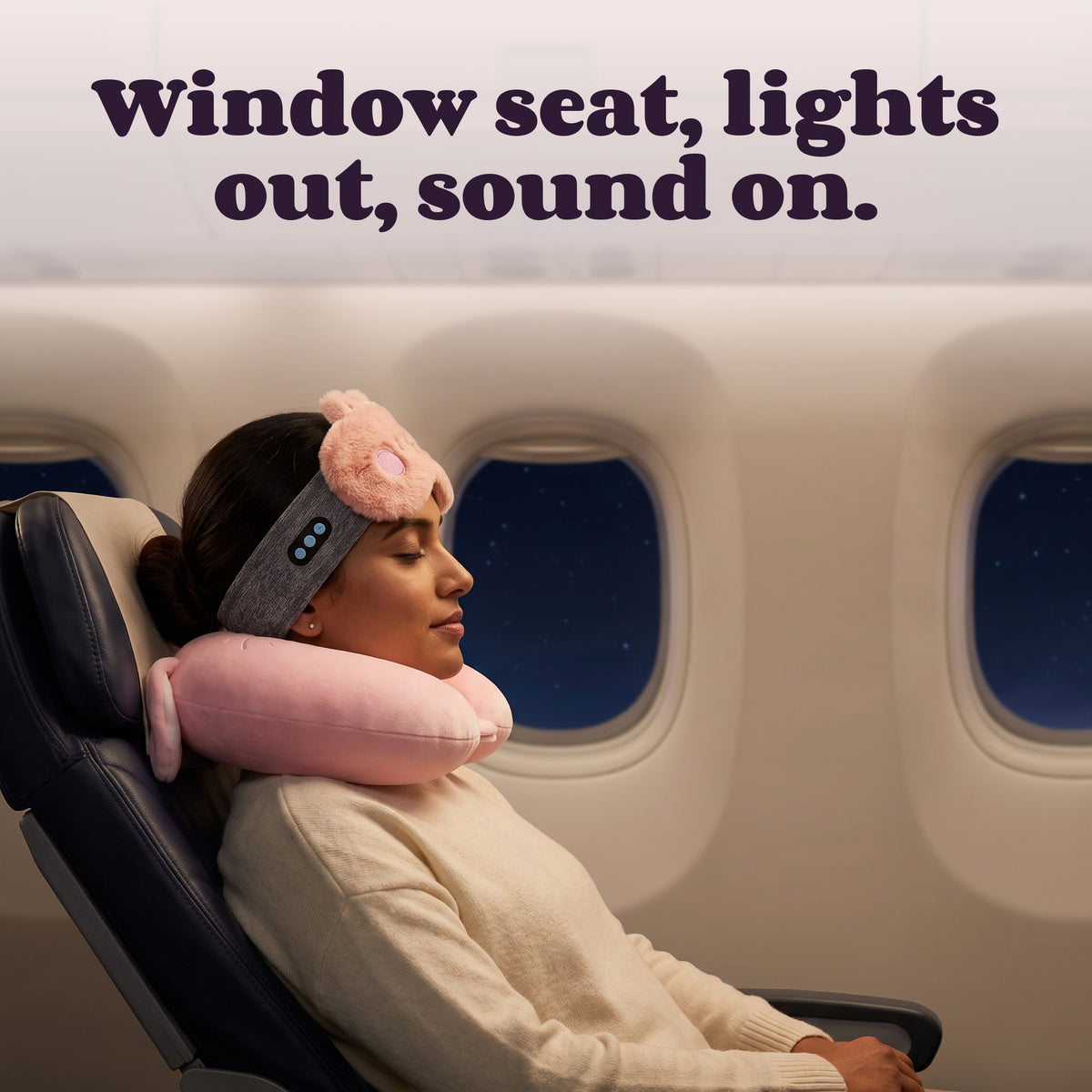 Woman on a night flight with The Red-Eye Kit – Window seat, lights out, sound on.