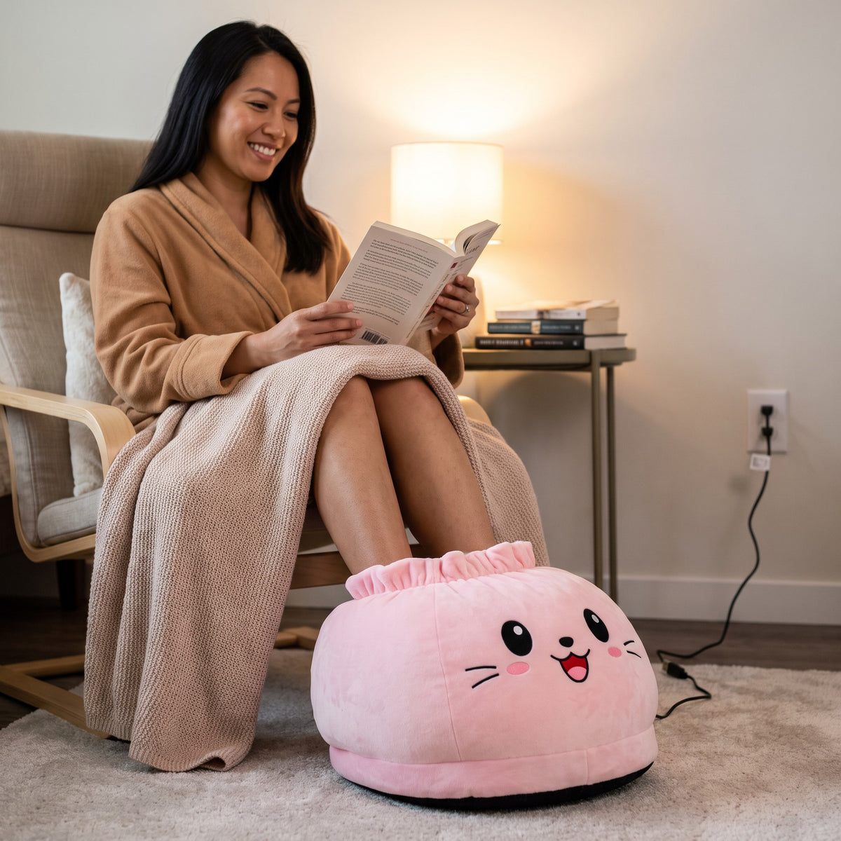 Woman reading in an armchair with her feet in the Snugglet Paw Warmer in Pink Smiley